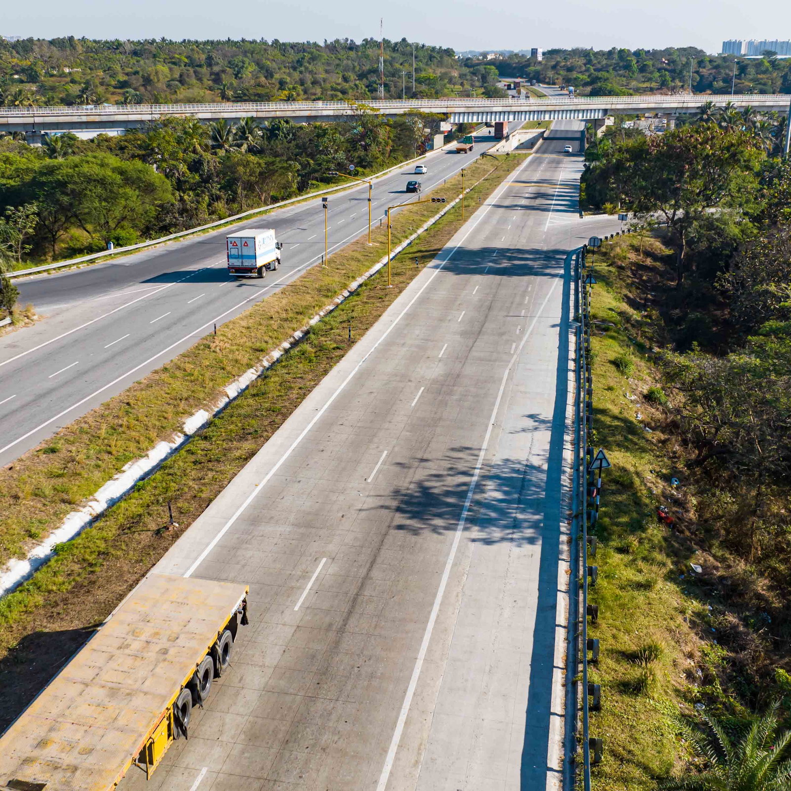 Square aerial view of a divided highway with sparse traffic and surrounding greenery