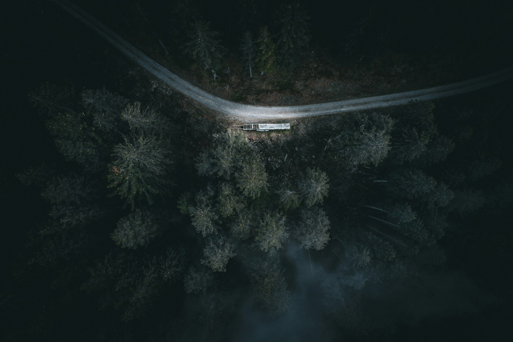Top-down aerial view of a remote road crossing dark forest