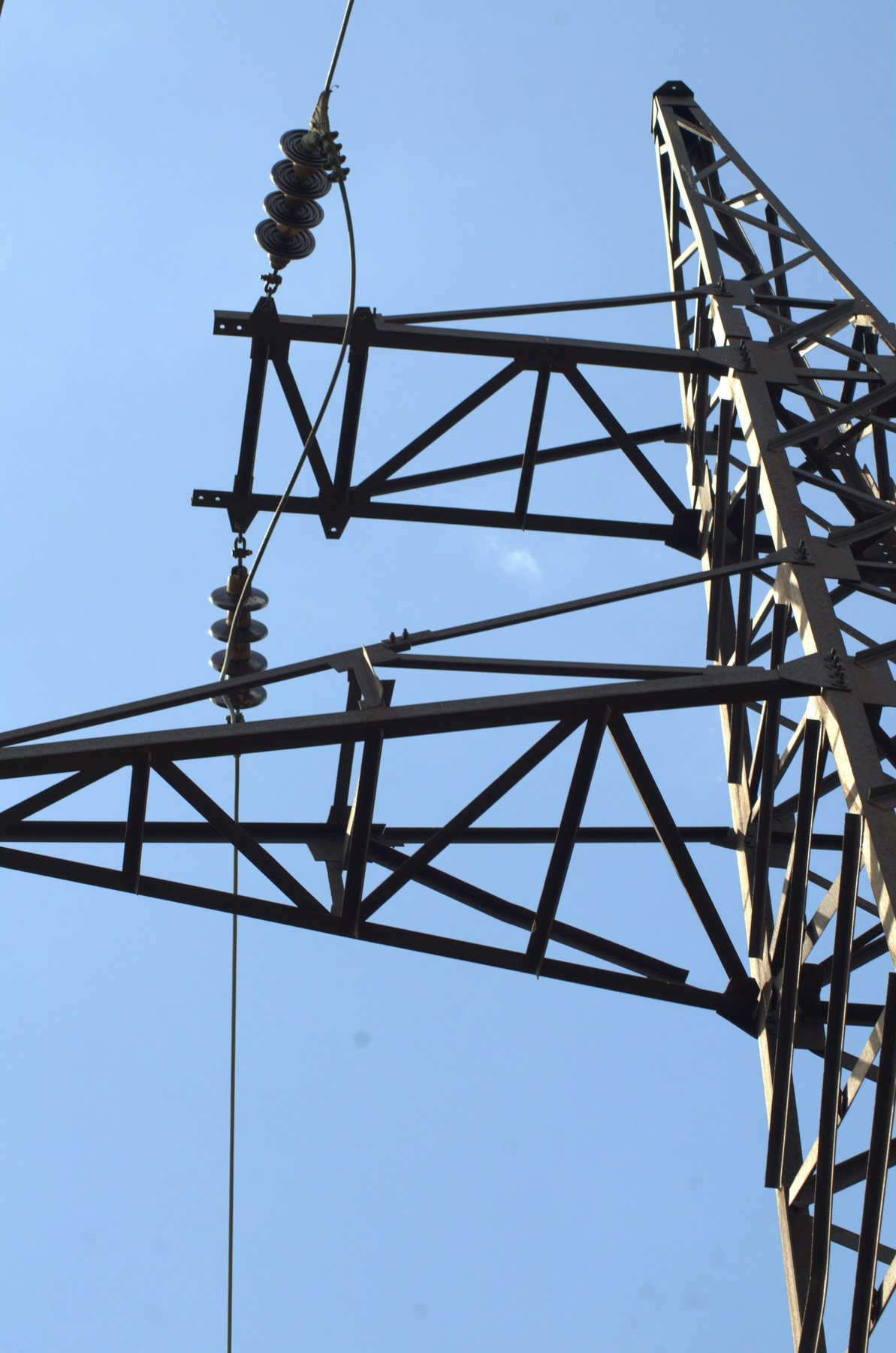 Close view of a steel transmission tower, conductor and suspended insulators against blue sky